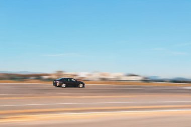 Otoyolda yüksek hızda giden bir araba var. Hız arkaplanı bulanık olan kahverengi bir sedanın yan görünümü.