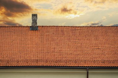 Gün batımında bulutlu bir gökyüzüne karşı turuncu kil kiremit çatı.