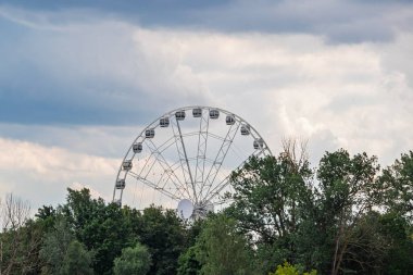 Ağaç tepelerinin arkasında büyük beyaz bir dönme dolap görünüyor..