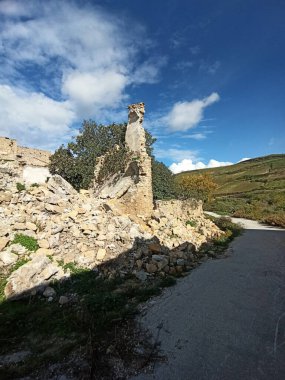 Görüntü, Sicilya 'daki Poggioreale harabelerinin canlı yeşillikler ve açık mavi gökyüzü ile kaplanmasını gösteriyor. Bu, tarihi yerlerin güzelliğini yansıtıyor.
