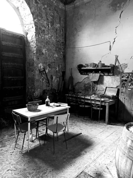 Poggioreale, Sicilya 'da terk edilmiş bir odada kırsal ahşap bir masa, sandalyeler ve klasik bir dekor sergileniyor ve tarihle dolu nostaljik bir atmosfer yaratıyor.