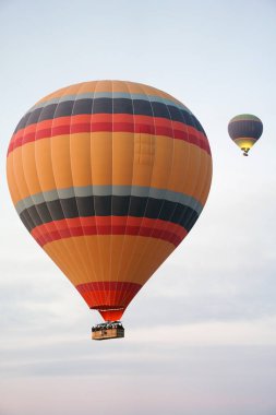 Güneş doğarken gökyüzünde uçan renkli sıcak hava balonları, sepetteki yolcularla bulutların üstünde manzaralı bir hava macerasının tadını çıkarıyorlar.