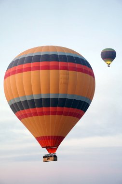 Güneş doğarken gökyüzünde uçan renkli sıcak hava balonları, sepetteki yolcularla bulutların üstünde manzaralı bir hava macerasının tadını çıkarıyorlar.
