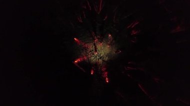 Dikey video. Bir adamın yalnız gölgesi gece ormanında ağaçların arasında duruyor. Kırmızı lambalar parlıyor ve bir ateş yanıyor. Hava görünümü.
