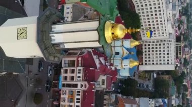 Dikey video. Ivano-Frankivsk 'teki Ermeni Kilisesi' nin havadan görünüşü ve Ukrayna bayrağıyla belediye binasının altın kubbesi..