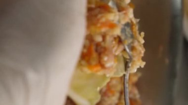 Dikey video. Şeflerin elleri beyaz eldivenli, elinde içi doldurulmuş bir lahana tutuyordu ve içine bir kaşık dolusu sos döküyordu. Kıyma kıyması, kıyma makinesinde kıvrılmış pirinç ve etten oluşur..