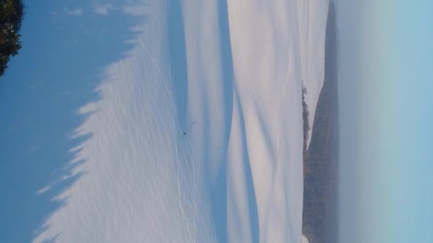垂直ビデオ 雪に覆われた日当たりの良いフィールド上のフライト 丘の長い影が見えます 無人機は一人旅の男に近づく 空中風景 — ストック動画