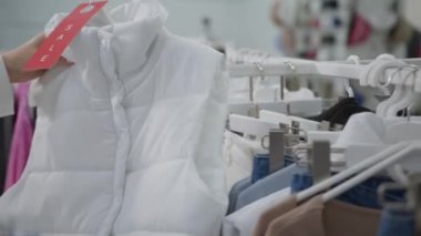Kadın eli beyaz kolsuz bir ceket tutuyor. Üstünde de kıyafet mağazasında indirim var..
