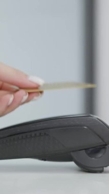 Dikey video. Beyaz bir arka planda cilalanmış manikürlü bir kadının eli NFC teknolojisi kullanarak ulaşılamaz bir kredi kartıyla ödeme yapıyor. Kablosuz para transferleri. Kablosuz ödeme.