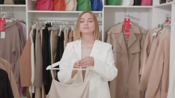白のビジネススーツの白人女性ブロンドは ストラップ付きアイボリーシルクのドレスを試着しています ファッションストアでのショッピング服 — ストック動画