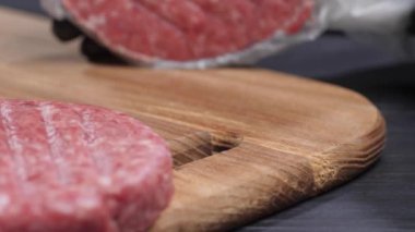 Yakın plan. Plastik torbayla kaplı hamburgerciden bir köfte düşüyor. Siyah eldivenli bir el bir alet tutar. Hamburger yapma süreci..