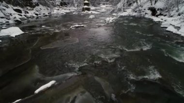 Bulutlu bir günde hızlı akan bir dağ kış nehrinin üzerinde uçmak. Kış manzarası.