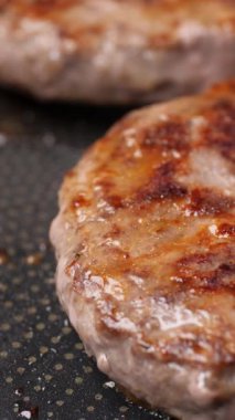 Dikey video. Burger pirzolaları siyah bir tavada kızartılıyor. Duman yükselir ve yağ akar. İştah açıcı kırmızı et hazırlanıyor. Kapat..