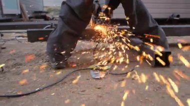 A worker cuts a metal profile with an angle grinder. Sparks fly into the camera lens in slow motion.
