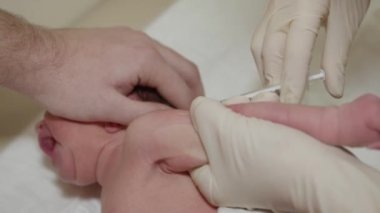 Yeni doğmuş bir çocuğun aşısı. Sol kolun ön koluna bir şırınga enjekte edilir. Beyaz eldivenli doktor yaklaş. Babaların eli bebeklerin başını tutar. Pediatri..