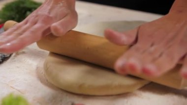The chefs female hands work with a wooden rolling pin, rolling it over a piece of dough. Production of products from flour. Bakery business.