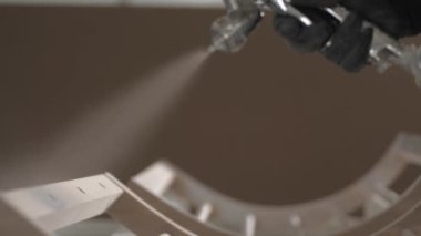 A carpenters hand applies primer and paint to a wooden surface. Painting wooden products with a brilliant spray gun in the carpentry workshop of a furniture factory.
