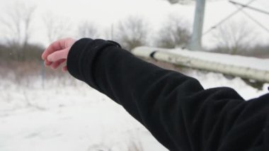 A hand in a black coat rises parallel to the planes wing and opens its palm against the background of falling snow in slow motion.