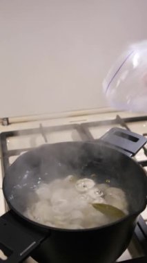 Dikey video. Donmuş hamur köfteleri plastik bir torbadan siyah bir tavada kaynar suya dökülür. Yarı bitmiş ürünlerin hazırlanması.
