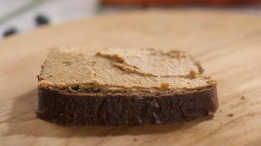 A hand takes a slice of black rye bread smeared with pate and takes it away from a wooden board. Close-up.