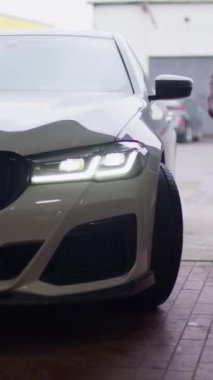Vertical video. A white passenger car slowly turns in front of the camera. You can see the left front side of the car, headlight, bumper, radiator, wheel. Visit to the maintenance service.