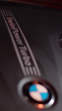 Lutsk, Ukraine - February 17, 2023: plastic black cover of the BMW 5 series engine with the inscription twin power turbo. Focus changes the sharpness to the emblem. A red moving light is shining.