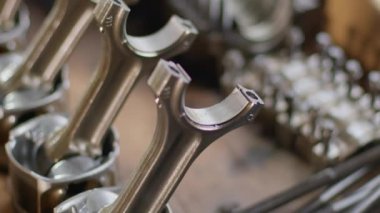 Pistons and connecting rods lie on the surface of the table. The transition of sharpness to the disassembled parts of the connecting rod with bolts and studs.