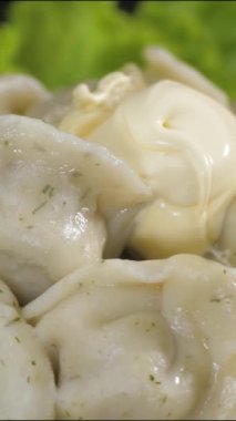 Vertical video. Dish of dumplings with meat in a glass plate, top with sour cream. The dish spins and stops. Close up.
