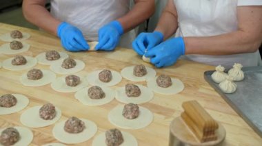 İki çift mavi eldivenli şefin elleri khinkali şeklindedir. Yarı bitmiş ürünlerin üretimi için hamur ve kıyma dolu büyük bir sanayi masası..