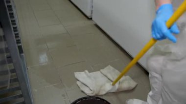 Sarı bir paspasla mavi eldivenli bir temizlikçi zemini gri fayanslarla kaplamış. Hijyen ve temizlik kavramı.