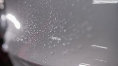 Kapatın. Arabanın gri parlak yüzeyine bir damla su damlatıyor. Aracın sol tarafındaki metal boyunca kamera kolu var..