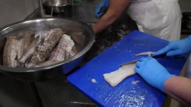 Eldivenli bir aşçının elleri kesme tahtasının üzerinde bir balık filetosunun omurgasını ve yüzgeçlerini bıçakla kesti. Yemek pişirme.