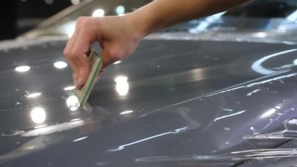閉めろ プラスチックスクレーパーを持つ女性の手は 灰色の新しい車のフードに保護抗砂利フィルムを接着します 特殊フィルムと車のボディ保護の概念 — ストック動画
