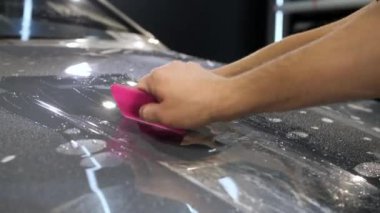 Plastik kazıyıcıları olan bir kadın ve bir erkek el gri yeni bir arabanın kaputuna koruyucu film yapıştırıyor. Kapatın. Araba vücut koruma kavramı.