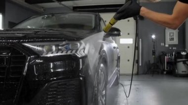 Profesyonel bir işçi, siyah bir cipin sol tarafını yüksek basınçlı bir yıkama makinesiyle yıkıyor. Araba temizliği ve temizlik..