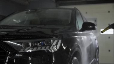 Bir oto yıkama işçisinin Bokeh eli bir oto yıkamada yüksek basınçlı çamaşır makinesiyle siyah bir arabanın sürücünün kapısını yıkar. Otomobilin tam önünde..