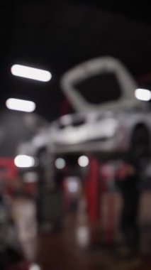 Dikey video. Bir işçi, kırmızı elektrikli asansörle yükselen gri bir araca teşhis koyuyor. Kaputu aç. Araba bakımı. Bulanık video odağından çıkarıldı.