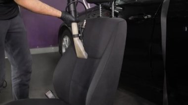 Bir işçi koltuğun arkasındaki kiri temizlemek için elektrikli süpürge kullanır. Arabanın iç kısmının profesyonel temizliği. Detaylandırma kavramı.