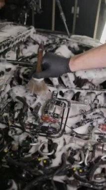 Dikey video. Fırçayla siyah eldivenli bir el motor elementlerini yıkar ve temizler. Silindir başındaki sabun köpüğü, hortumlar, kablolar. Araba temizleme kavramı.