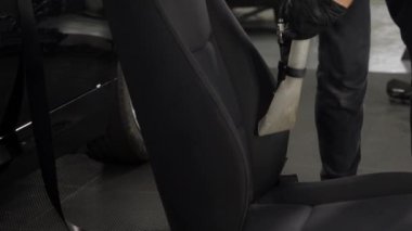 Araba yıkamada çalışan bir işçi koltuğun arkasındaki kiri temizlemek için elektrikli süpürge kullanır. Arabanın iç kısmının profesyonel temizliği. Detaylandırma kavramı.