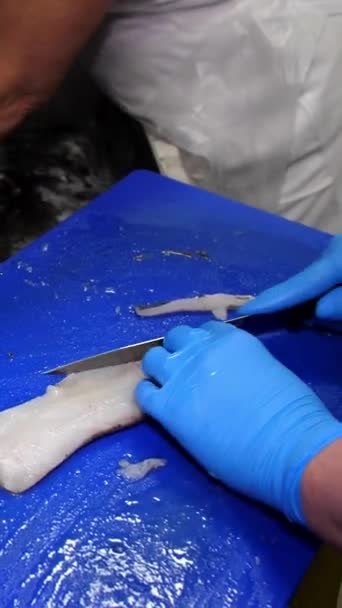 バーティカルビデオ 切断ボードの手袋で調理した手袋の手は ナイフで海の魚のフィレットからバックボーンとフィンを切りました クッキングミール — ストック動画