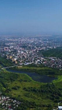 Dikey video. Ukrayna 'nın batısındaki bir Ukrayna şehri üzerinde uçuş. Çevrede binalarla çevrili yeşil bir nehir var..