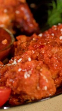 Dikey video. Renkli manikürlü kadın parmaklar masadaki bir kaseden tavuk kanadı alır. Fast food, dereotu ve susam tohumlu tabak..