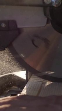 Dikey video. Dairesel testere tahta keser. Güneş ışığıyla aydınlatılan bir çip havada uçuyor. Yavaş çekim. Ahşap Çalışması.