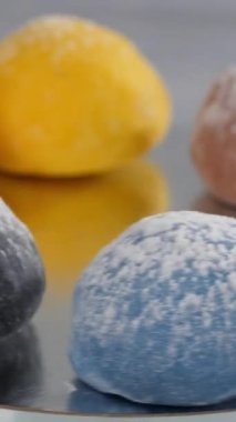 Dikey video. Karamel, armut, ahududu, erik, mango ve fıstık aromalı altı mochi keki ayna yüzeyinde yatarken dönüyor. Japon geleneksel mutfağı.