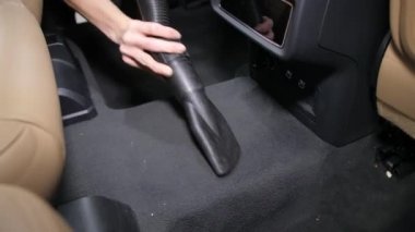 Kapatın. Bir kadın eli elektrikli süpürge hortumunu tutar ve arabanın içini koltuklar arasında vakumlar. Ayrıntılı hizmetler.
