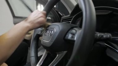 Lutsk, Volyn / Ukrayna - 10 Haziran 2023: Bir kadının eli, bir Audi arabasının direksiyonundaki tozu fırçayla süpürür. Sürücü koltuğu ve dört yüzüğün amblemi. Ayrıntılı hizmetler.