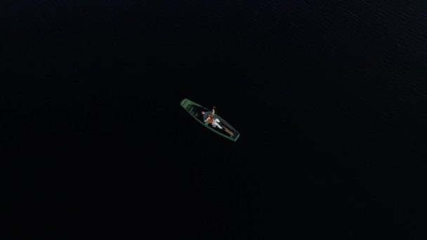 男は木製のボートに横たわるギターを演じ 波の中の太陽のわずかな反射で水の上の野生湖の真ん中にいる エアリアルビュー — ストック動画