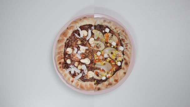 在粉红盘上的白色背景上旋转的两种巧克力披萨的分屏 从表面上看 从榛子 棉花糖 椰子屑 梨子和奶油中提取的原料 — 图库视频影像