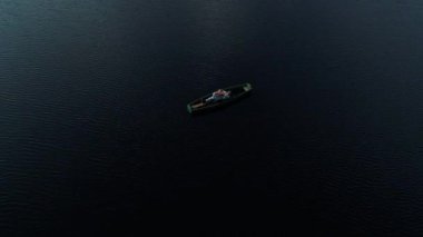 Bir adam, güneş ışığıyla birlikte, vahşi bir gölün ortasında, tahta bir teknede gitar çalar. Hava görünümü.